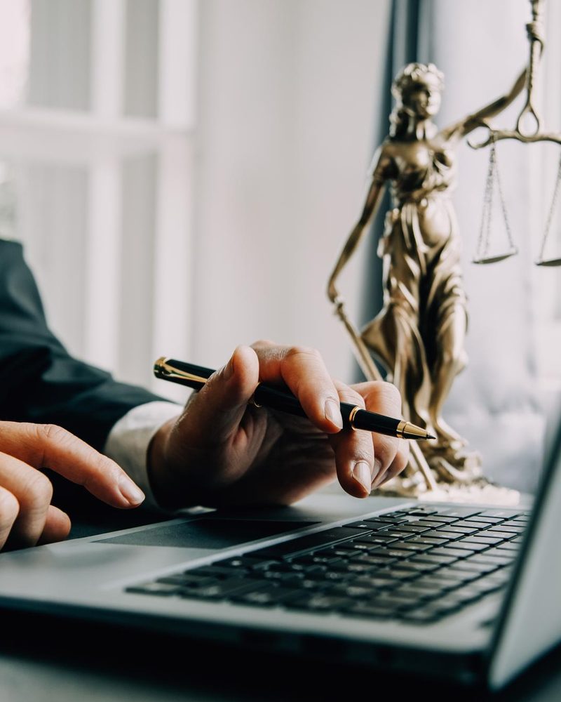 Profissional trabalhando no notebook ao lado de uma estátua da justiça